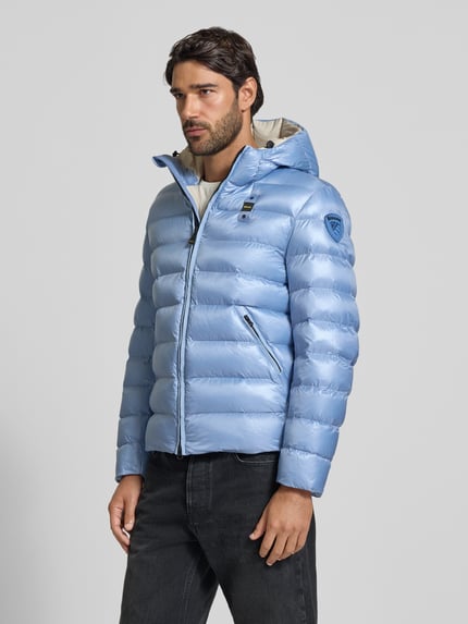 Männermodel trägt Steppjacke mit Zweiwege-Reißverschluss Modell 'ADAMS' von Blauer USA in Hellblau, glänzende Textur, Ganzkörperansicht von vorne. Regular Fit, Kapuze mit Tunnelzug, Label-Detail, Größe M.