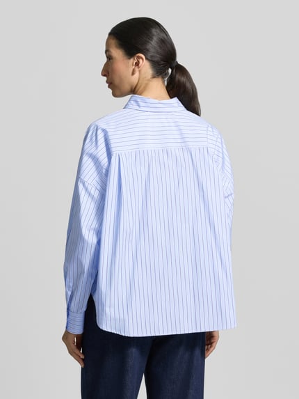 Frauenmodel trägt Oversized Hemdbluse aus reiner Baumwolle Modell 'AUREO' von Weekend Max Mara, blau-weiß gestreift, Ganzkörperansicht Rückansicht.