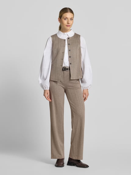 Frauenmodel trägt Weste mit Viskose-Anteil Modell 'Bonnie' von FREE/QUENT in Beige mit Knopfleiste, taillierte Passform, Ganzkörperansicht von vorne. Elastischer Material-Mix, sichtbare Struktur, Kombination mit weißer Bluse und Hose, Kontext: Rückenlänge 52 cm, Schulterbreite 36 cm, Brustweite 48 cm bei Größe S.