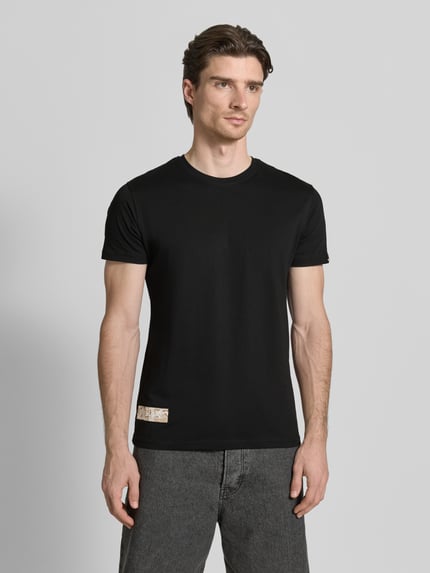 Męski model nosi czarne T-Shirt mit Label-Patch Modell 'Camo' od Alpha Industries z bawełny woskowanej, krój prosty, widok całej sylwetki z przodu.