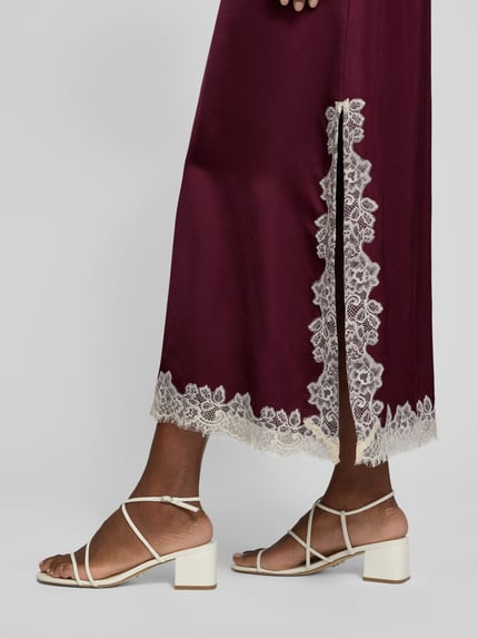 Kobiece modelka nosi długa sukienka z wiskozy z obszyciem koronką od Jake*s Collection, bordowy kolor, detal boczny, długość tyłu w rozmiarze 36: 133 cm, szerokość w rozmiarze 36: 52 cm, długość rękawów w rozmiarze 36: 13 cm, detaliczne ujęcie dolnej części sukienki.