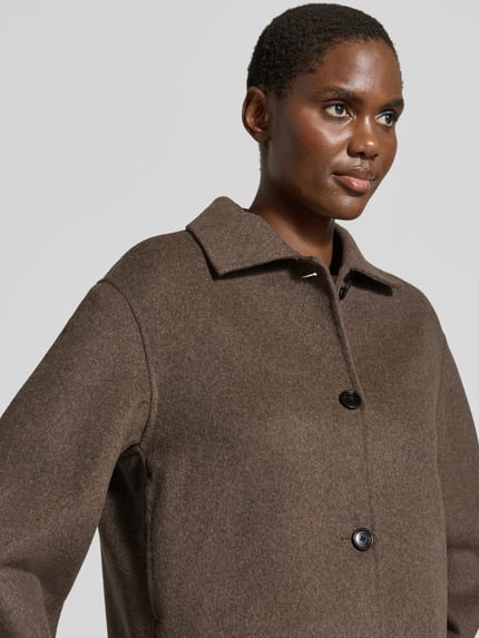 Frauenmodel trägt Jacke aus Woll-Mix Modell 'ALEX' von MANGO in Braun mit Umlegekragen und Knopfleiste, Nahaufnahme Oberkörper.