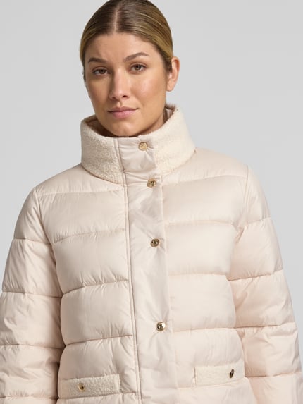 Kobiece modelka nosi kurtkę pikowaną z jasnego materiału, model 'Olmina' od JOOP!, kurtka ze stójką, krój regular fit, zbliżenie na górną część ciała.