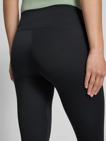 Frauenmodel trägt Tights mit elastischem Bund und Logo von NIKE TRAINING, schwarzer Material-Mix mit Stretch, Nahaufnahme Rückansicht.