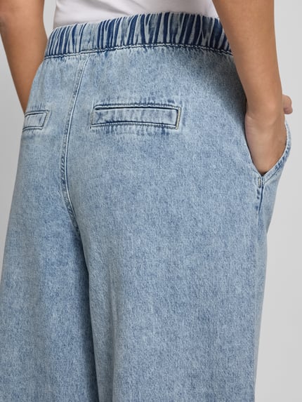 Männermodel trägt Wide Leg Jeans aus Baumwoll-Viskose-Mix Modell 'VALERIA' von Vero Moda, stylizowana na denim, elastyczny ściągacz, boczne wpuszczane kieszenie, z przodu imitacja kieszeni z tyłu, detal materiału, mieszanka bawełny i wiskozy, zdjęcie: detailaufnahme tyłu.