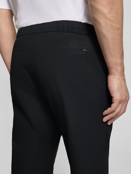 Männermodel trägt Slim Fit Schlupfhose mit Gesäßtasche von CK Calvin Klein in Schwarz, elastischer Bund, Detailaufnahme Rückansicht.