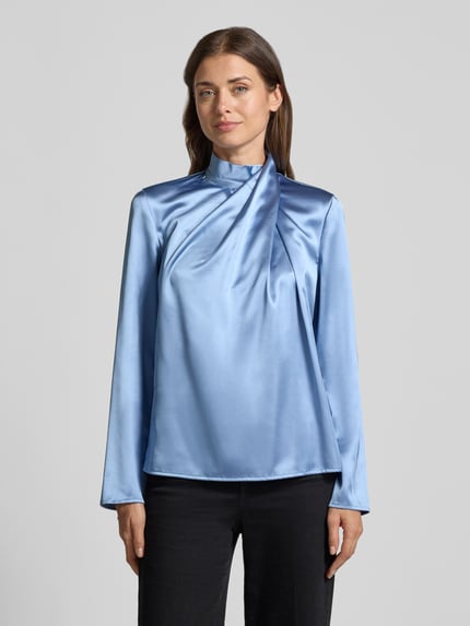 Modelka kobieca ma na sobie Regular Fit Langarmbluse aus Satin von Jake*s Collection w jasnoniebieskim kolorze o gładkiej, błyszczącej fakturze, kontrast z czarnymi spodniami, widok całej sylwetki z przodu.