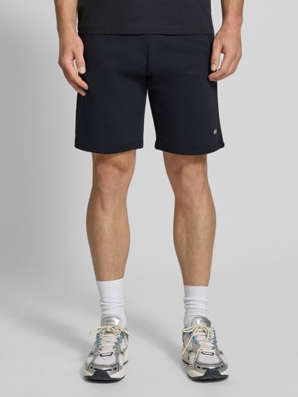 Männermodel trägt Sweatshorts mit Eingrifftaschen van Christian Berg Men in donkerblauw, puur katoen, regular fit, labeldetail, ganzkörperansicht von vorne.