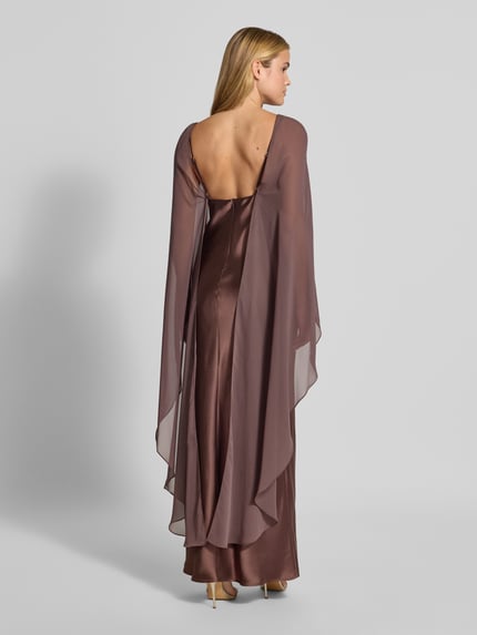 Männermodel trägt długa sukienka z satyny Maxikleid aus Satin von SWING, elastyczna mieszanka materiałów, dopasowany krój, półprzezroczysta etola, cienkie ramiączka, dekolt w serek, długość tyłu w rozmiarze 36: 133 cm, szerokość w rozmiarze 36: 31 cm, brązowe odcienie, matowa i błyszcząca tekstura, całkowity widok z tyłu