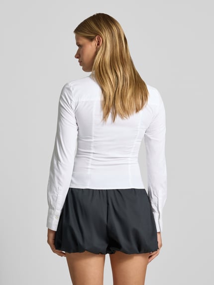 Vrouwenmodel draagt witte overhemdblouse met knoopsluiting van REVIEW, katoenmix met stretch, getailleerd model, sportmanchet, afgeronde zoom, overhemdkraag, mouwlengte maat S 55 cm, zwart short, Ganzkörperansicht Rückansicht.