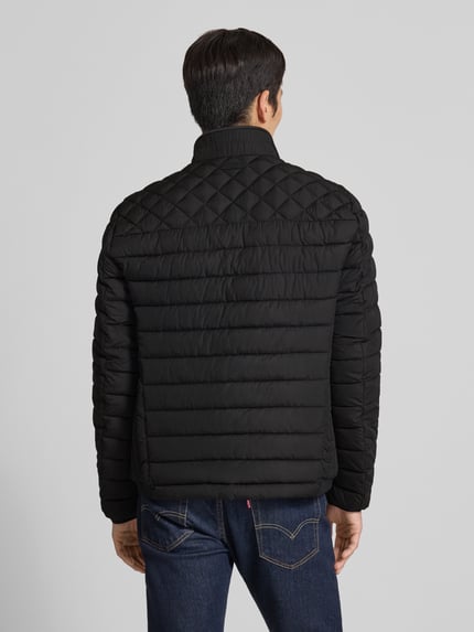 Męski model nosi Slim Fit Steppjacke mit gefüttertem Kragen von Christian Berg Men, czarny kolor, krój slim fit, poziome pikowanie, elastyczne zakończenia rękawów, kieszenie zapinane na zamek błyskawiczny, długość tyłu w rozmiarze M: 68 cm, szerokość ramion w rozmiarze M: 47 cm, szerokość w rozmiarze M: 52 cm, długość rękawów w rozmiarze M: 68 cm, widok całej sylwetki z tyłu.