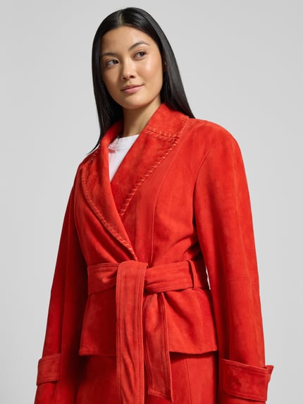 Frauenmodel trägt Lederjacke mit Bindegürtel von Marc Cain aus Echtem Leder, taillierter Schnitt, Reverskragen, leuchtendes Rot, Nahaufnahme Oberkörper.