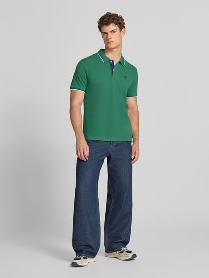 Mannelijk model draagt Slim Fit Poloshirt met Label-Stitching van CHAMPION in groen, puur katoen, knoopsluiting, ruglengte maat M 73 cm, ganzlichaamsaanzicht van voren.