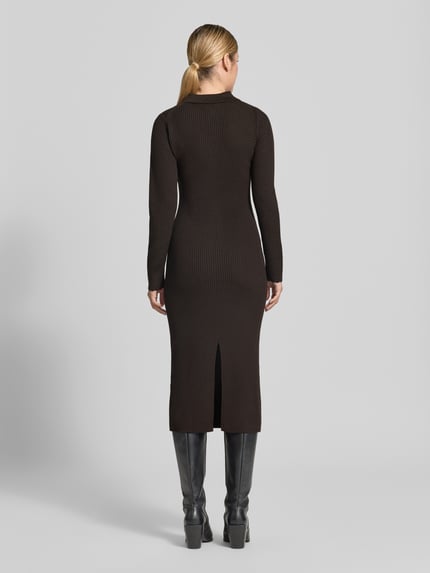 Frauenmodel trägt figurbetontes, schwarzes Strickkleid mit Polokragen und Knopfleiste Modell 'AMARILA' von DRYKORN, Ripp-Optik, Ganzkörperansicht Rückansicht.