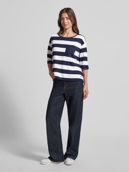 Frauenmodel trägt Relaxed Fit Sweatshirt aus Viskose-Mix mit Brusttasche von monari, marineblau-weiß gestreift, Halbarm, Rundhalsausschnitt, Logo-Stitching, lässige Passform, weiche Textur, kombiniert mit dunkler Jeans, Ganzkörperansicht von vorne.