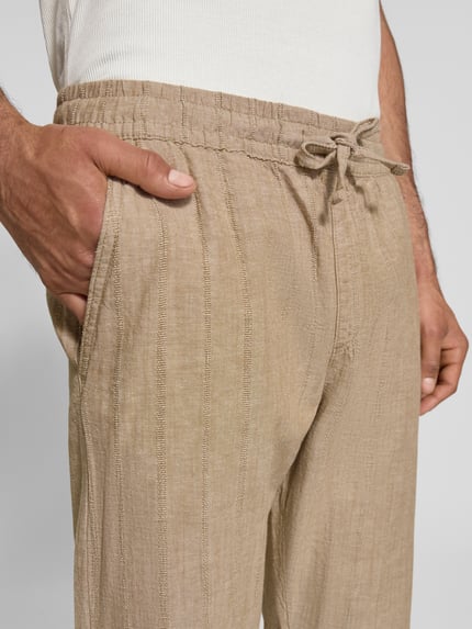 Mężczyznamodel nosi spodnie Relaxed Fit Hose aus Baumwoll-Leinen-Mix Modell 'KANE' von Jack & Jones, kolor beżowy, tekstura delikatna, tunel, elastyczny pas, kieszeń z tyłu; mieszanka bawełny i lnu, szerokość w rozmiarze M: 41 cm, długość wewnętrzna nogawki w rozmiarze M: 77 cm, zbliżenie na górną część przodu.