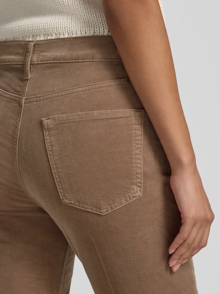 Kobieta nosi Regular Fit Gerade Hose aus Baumwoll-Mix Modell 'MAY S' od BRAX, kolor jednolity beżowy, sztruks, detal z metką, pięć kieszeni, bawełniany miks, zapięcie na guzik i ukryty zamek, szlufki na pasek, detaliczny widok tylnej kieszeni, zbliżenie na biodra.