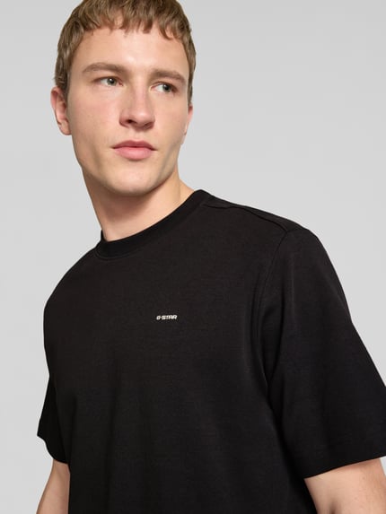 Männermodel trägt Regular Fit T-Shirt mit Logo-Print Modell 'True' von G-Star Raw in Schwarz, Rundhalsausschnitt, Nahaufnahme Oberkörper. Rückenlänge bei Größe M: 66 cm.