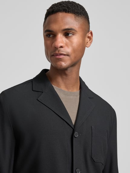 Männermodel trägt Relaxed Fit Hemdjacke mit Viskose-Anteil Modell 'Bill' von DIGEL in Schwarz, strukturierte Oberfläche, Nahaufnahme Oberkörper. Elastischer Material-Mix, Reverskragen, aufgesetzte Tasche, Knopfleiste.