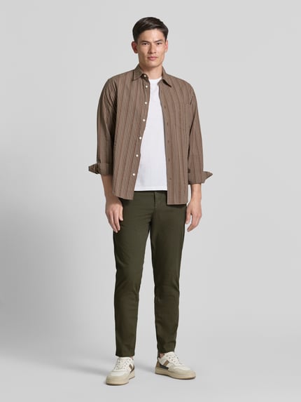 Männermodel trägt Tapered Chino aus Baumwoll-Mix Modell 'CHINO-TAPERED-DS-10' von BOSS Orange in Olivgrün, unifarben, Ganzkörperansicht von vorne. Kontext: Tapered Passform, elastischer Bund, Knopfverschluss, seitliche Eingrifftaschen, Gesäßtaschen, innen oder außen tragbarer Tunnelzug.