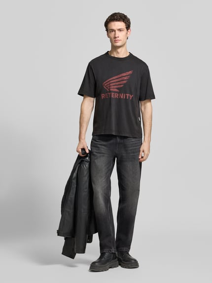 Męski model trägt t-shirt z nadrukiem z logo Model 'AÉRO' von RETERNITY, czarna bawełna, krój regular fit, okrągły dekolt, długość tyłu w rozmiarze M: 67 cm, Ganzkörperansicht von vorne