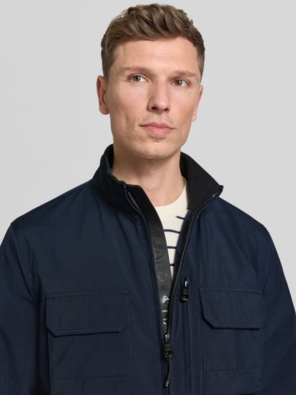 Männermodel trägt Jacke met opstaande kraag van NAUTGÅRD, regular fit, ritssluiting, steekzakken, borstzak, maat M, nahaufnahme bovenlichaam.