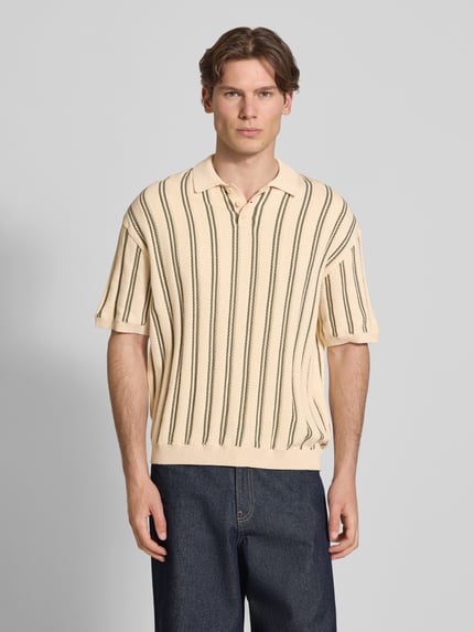Männermodel trägt Regular Fit Strick-Poloshirt Modell 'POUL' von Redefined Rebel aus Baumwoll-Mix, creme mit dunklen Längsstreifen, Knopfleiste, Rückenlänge bei Größe M 66 cm, Ganzkörperansicht von vorne.