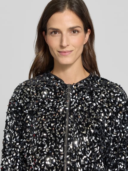 Frauenmodel trägt Bomberjacke mit Paillettenstruktur Modell 'VMBELLE' von VERO MODA, glänzende Metallic-Optik, Nahaufnahme Oberkörper.