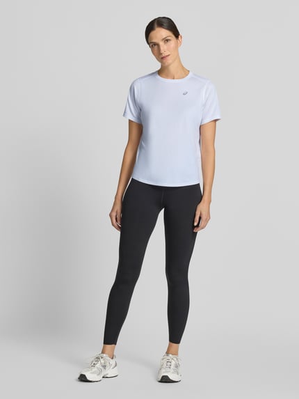 Frauenmodel trägt T-Shirt mit Rundhalsausschnitt und Logo-Print von ASICS in Hellblau, glatte Struktur, dezenter Print, Ganzkörperansicht von vorne, Damen T-Shirt, gerader Schnitt, leicht abgerundeter Saum, Rückenlänge 60 cm bei Größe S