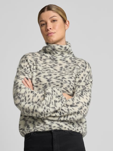 Frauenmodel trägt Oversized Turtleneck-Pullover aus Woll-Mix von ARMEDANGELS, creme mit grauem Muster, weiche Textur, Nahaufnahme Oberkörper.