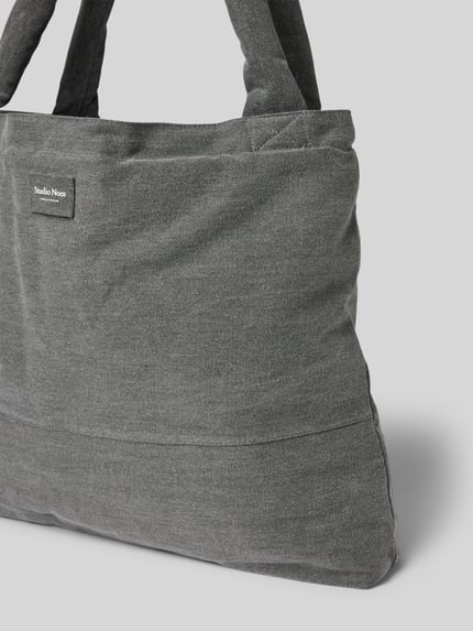 Produktfoto, Tote Bag aus reiner Baumwolle in Denim-Optik von Studio Noos, detal z logo, szerokość w rozmiarze 1: 60 cm, długość: 42 cm, głębokość: 9 cm, długość paska na ramię: 75 cm, otwarta przegródka, pasek na ramię, tkanina stylizowana na denim
