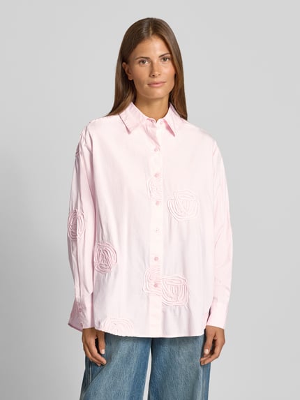 Frauenmodel trägt Regular Fit Hemdbluse aus reiner Baumwolle Modell 'Dalma Doris' von Neo Noir, rosa mit floralem Allover-Besatz, Nahaufnahme Oberkörper.
