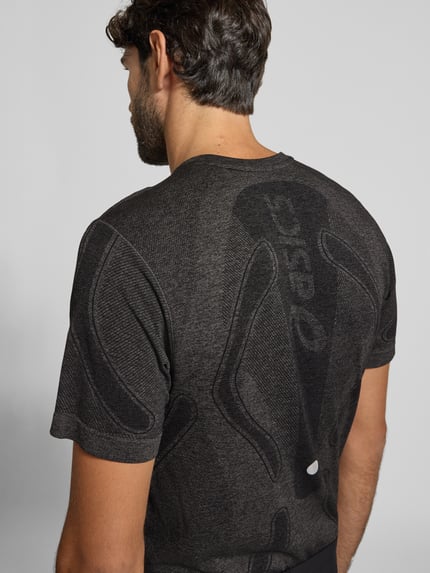 Męski model nosi męski t-shirt Slim Fit RUNNING T-Shirt Model 'ROAD' od ASICS w kolorze antracytowym z nadrukiem z logo z efektem metalicznym, okrągły dekolt, długość tyłu w rozmiarze M: 72 cm, widok na plecy, zdjęcie całej sylwetki z tyłu.