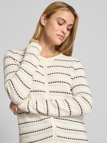 Kobiece modelka nosi Regular Fit Jacke aus reiner Baumwolle in Strick-Optik von Christian Berg Woman, kremowe tło, perforowanie, imitacja dzianiny, listwa guzikowa, długi rękaw, Długość tyłu w rozmiarze S: 60 cm, Długość rękawów w rozmiarze S: 65 cm, zbliżenie na górną część ciała.