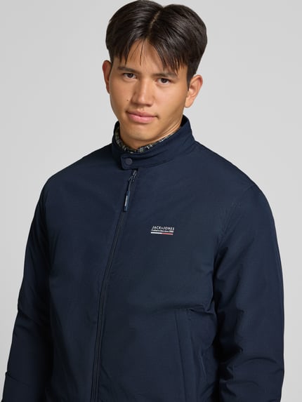 Männermodel trägt donkerblauwe bomberjack met opstaande kraag, Logo en ritssluiting, Model 'BROOKLYN' van JACK & JONES, regular fit, Nahaufnahme Oberkörper. Ruglengte maat M: 67 cm, schouderbreedte: 49 cm, borstwijdte: 59 cm, mouwlengte: 66 cm.