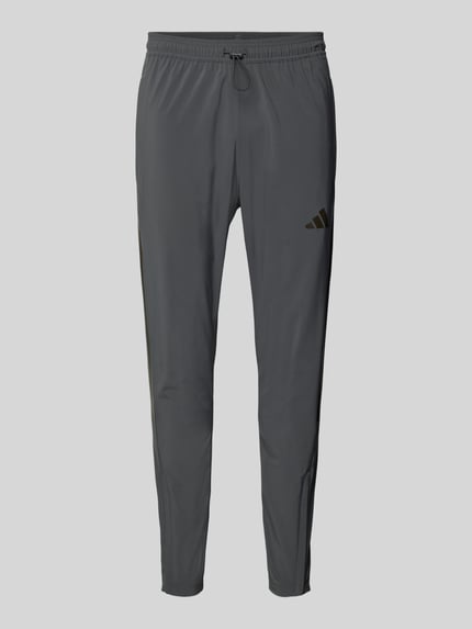 Produktfoto, Regular Fit Jogpants mit elastischem Bund Modell 'TIRO' von adidas Sportswear, krój regular fit, elastyczna tkanina, szary kolor, boczne kieszenie, suwak na dole nogawek, długość nogawki w rozmiarze M: 71 cm