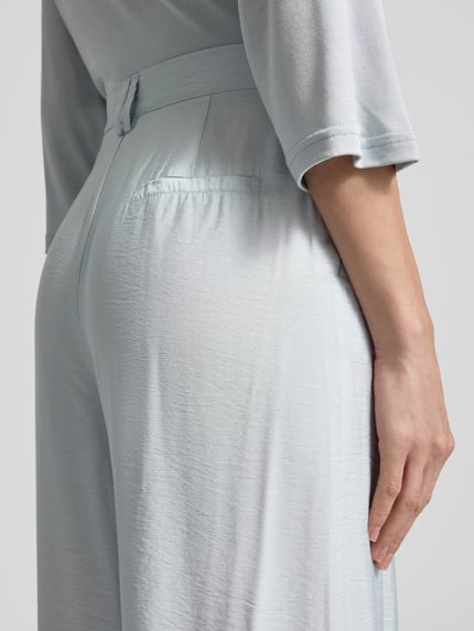 Vrouwenmodel draagt lichte wide fit stoffen broek model 'FINJA' van GUIDO MARIA KRETSCHMER WOMAN met steekzakken, detailopname zijkant. Context: dames stoffen broek van GUIDO MARIA KRETSCHMER WOMAN, wide fit, vloeiende stof, model 'FINJA', steekzakken, bandwijdte bij maat 36: 36 cm, binnenbeenlengte bij maat 36: 78 cm.