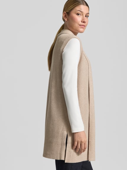 Frauenmodel trägt Strickweste aus Viskose-Mix mit offener Front von Christian Berg Woman, beigefarbene Feinrippstruktur, Straight Fit, Rückenlänge 77 cm, Ganzkörperansicht Rückansicht.