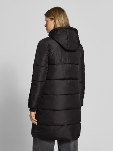 Frauenmodel trägt Puffermantel mit Kapuze von PIECES in Schwarz, Longline-Optik, Teilungsnähte, Reißverschluss, Taschen, Kapuze, Ganzkörperansicht Rückansicht.