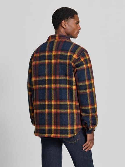 Męski model nosi koszulę casualową Regular Fit Model 'Hunter Arch™' od Columbia, kraciasty wzór w odcieniach granatu, żółci i czerwieni, detal z logo, kołnierzyk typu kent, długie rękawy, listwa guzikowa, Szerokość ramion w rozmiarze M: 43 cm, Długość tyłu w rozmiarze M: 76 cm, Szerokość w rozmiarze M: 60 cm, Długość rękawów: 73 cm, widok całej sylwetki z tyłu.