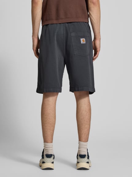 Männermodel trägt Herren Shorts mit Gesäßtasche Modell 'Floyde' von Carhartt Work In Progress aus Lyocell-Mix, Loose-Fit, dunkel, Ganzkörperansicht Rückansicht