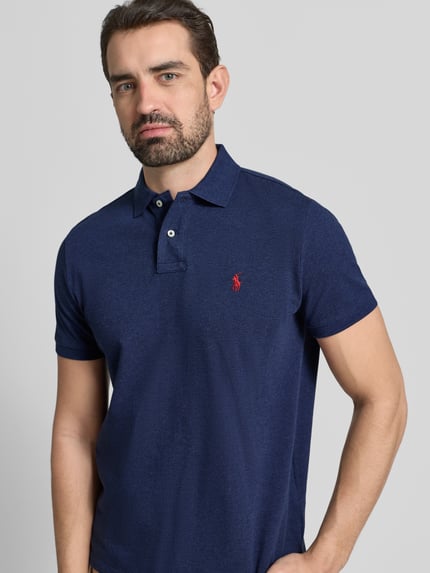 Męski model nosi Koszulkę polo z wyhaftowanym logo Polo Ralph Lauren z bawełny, krój regular fit, kołnierzyk polo, listwa guzikowa, granatowy kolor, prążkowane zakończenia rękawów, długość tyłu 68 cm w rozmiarze M, półzbliżenie tułowia z przodu.