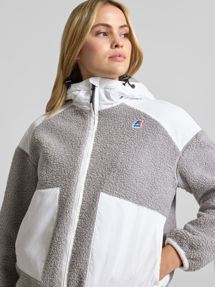 Frauenmodel trägt Teddyjacke mit Label-Detail und Zweiwege-Reißverschluss von K-WAY in Grau und Weiß, verschiedene Texturen, Nahaufnahme Oberkörper. Regular Fit, Kapuze mit Tunnelzug, sichtbare Taschen, Kontextdaten: Rückenlänge 62 cm, Schulterbreite 58 cm, Brustweite 58 cm, Ärmellänge 52 cm.