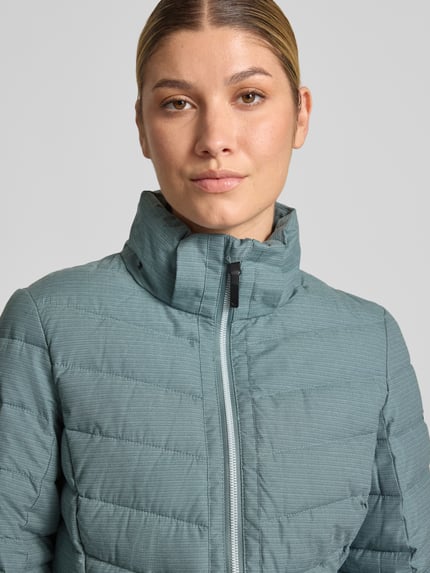 Frauenmodel trägt Jacke mit Kapuze und Label-Patch Modell von G.I.G.A. DX in Türkis mit Steppmuster, Nahaufnahme Oberkörper.