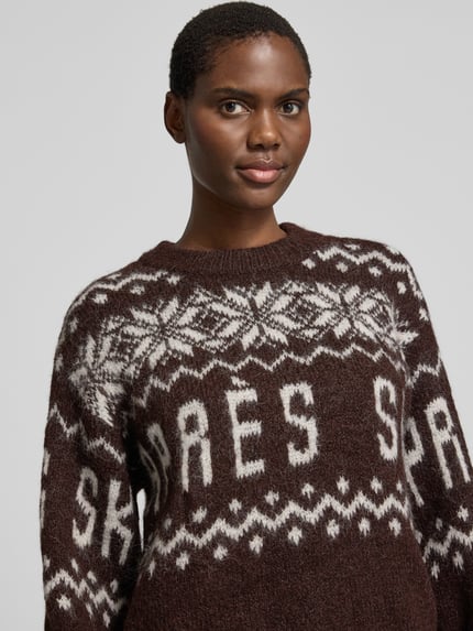 Frauenmodel trägt Pullover mit Ballonärmeln von VERO MODA, Jacquard-Strickoptik, geometrisches Allover-Muster, Nahaufnahme Oberkörper.