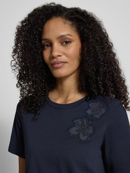 Vrouwenmodel draagt T-shirt met florale applicaties en ronde hals van Christian Berg Woman Selection, mix van katoen en elastaan, regular fit, ruglengte bij maat 36: 55 cm, detailopname bovenlichaam.