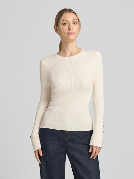Frauenmodel trägt Slim Fit Longsleeve aus Viskose-Mix Modell 'Ellie' von GUESS mit Strasssteinbesatz und Logo-Detail, Nahaufnahme Oberkörper.