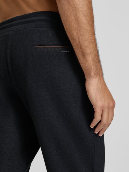 Männermodel trägt Sweatpants mit elastischem Bund und Tunnelzug von bugatti aus Baumwoll-Mix, krój regular fit, Eingrifftaschen, kolor czarny, tekstura miękka, detal tylnej kieszeni, detalaufnahme Bereich Hüfte