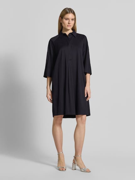 Frauenmodel trägt Hemdblusenkleid mit überschnittenen Schultern von Marc Cain, dunkle Farbe, Baumwolle mit Viskose-Anteil, Gerader-Schnitt, 3/4-Arm, Hemdblusenkragen, verdeckte Knopfleiste, Label-Detail, Rückenlänge 101 cm, Brustweite 53 cm, Ärmellänge 48 cm, Ganzkörperansicht von vorne.