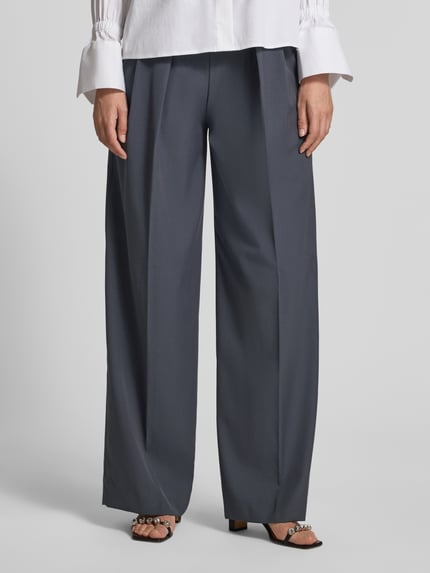 Frauenmodel trägt Wide Fit Hose mit Viskose-Anteil Modell 'Dario' von MANGO, Bundfalten, dunkelgrau, glatte Textur, Nahaufnahme Unterkörper.